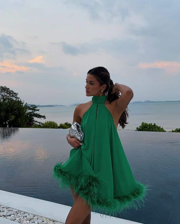 Woman in a green dress by an infinity pool with ocean view at sunset.