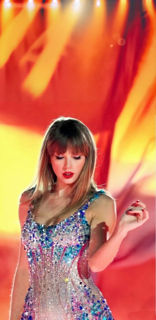 Singer in sparkling dress performing on stage with vibrant red and orange lighting.