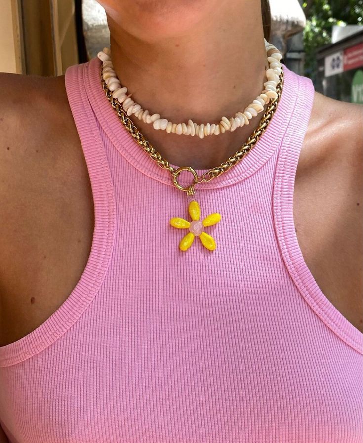 Woman in pink tank top wearing shell necklace and yellow daisy pendant, close-up view.