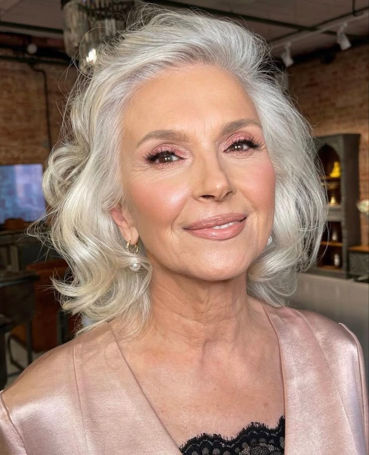 Elegant mature woman with silver hair and radiant smile wearing a blush pink outfit.