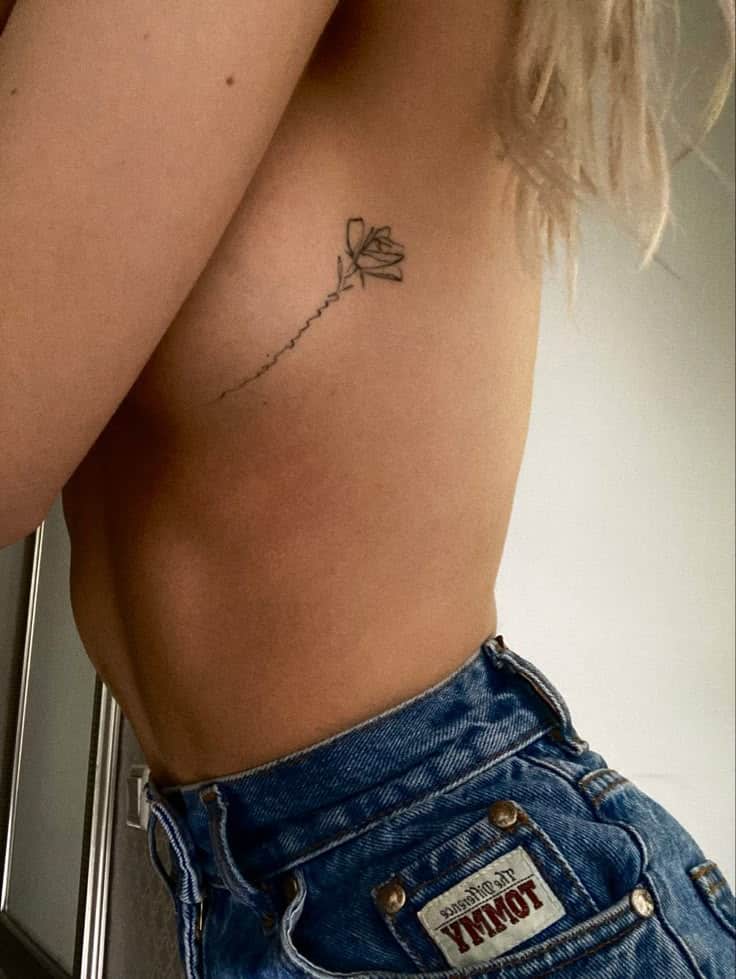 Side view tattoo of a delicate flower on a person's ribcage with blue denim jeans visible.