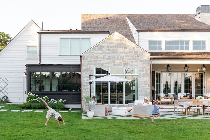 Spacious backyard with family relaxing and playing on the lawn in front of a modern, stone-clad house.