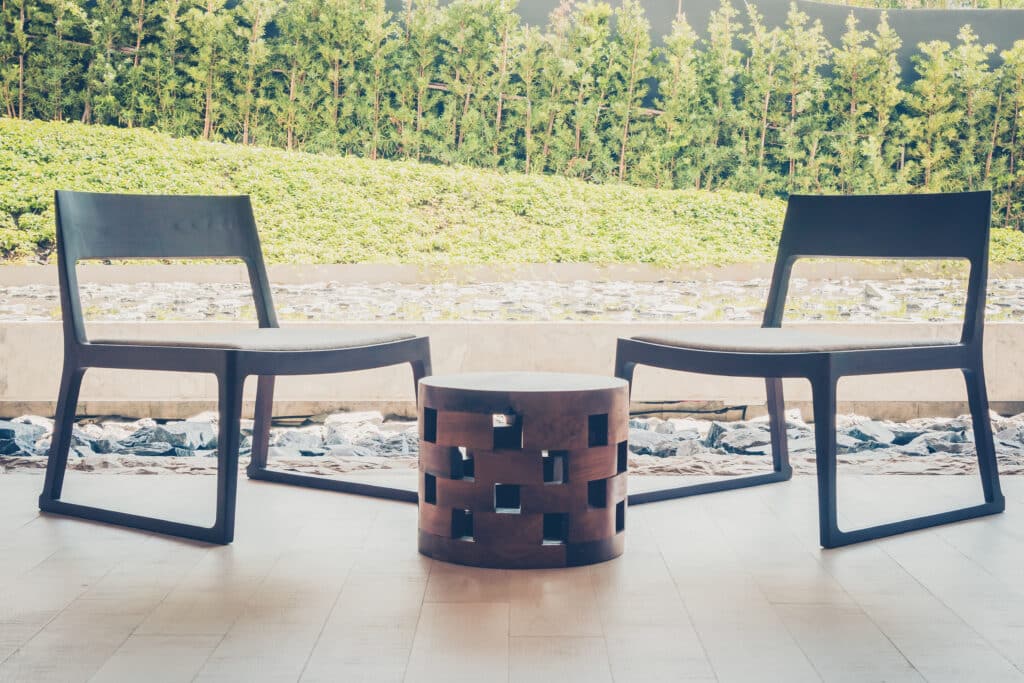 Modern outdoor lounge area with two wooden chairs and a small table, surrounded by greenery.