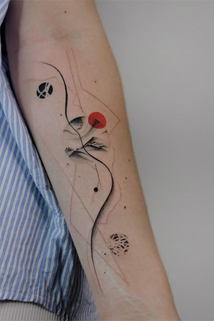 Abstract geometric tattoo with red, black, and gray elements on a forearm, featuring lines and circular patterns.