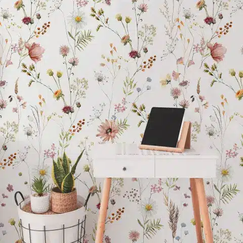Floral wallpaper backdrop with a small desk, two potted plants, and a tablet on a wooden stand for a cozy workspace.
