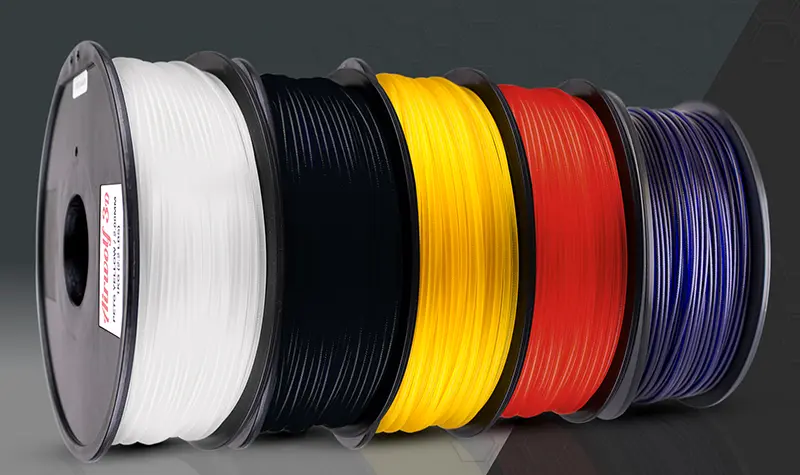 Colorful spools of 3D printer filament: white, black, yellow, red, blue on a dark background.