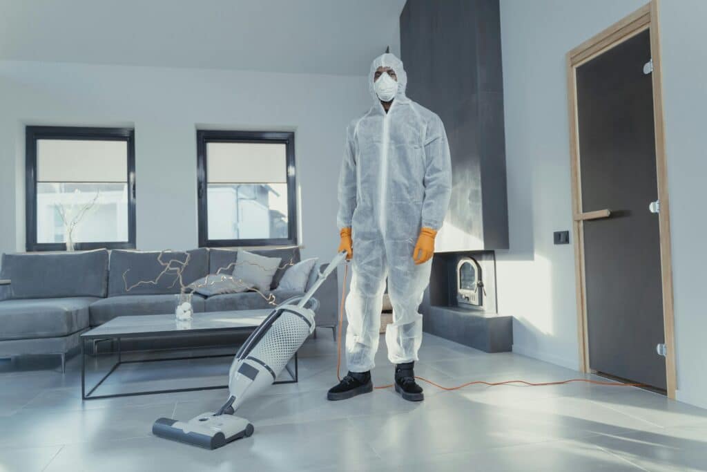 Person in protective gear vacuuming a modern living room for deep cleaning.