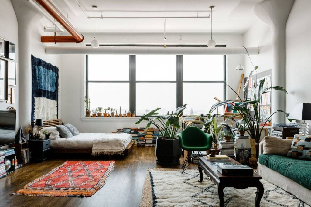 Stylish loft apartment with cozy bedroom, plants, large windows, and vibrant decor for a modern urban living experience.