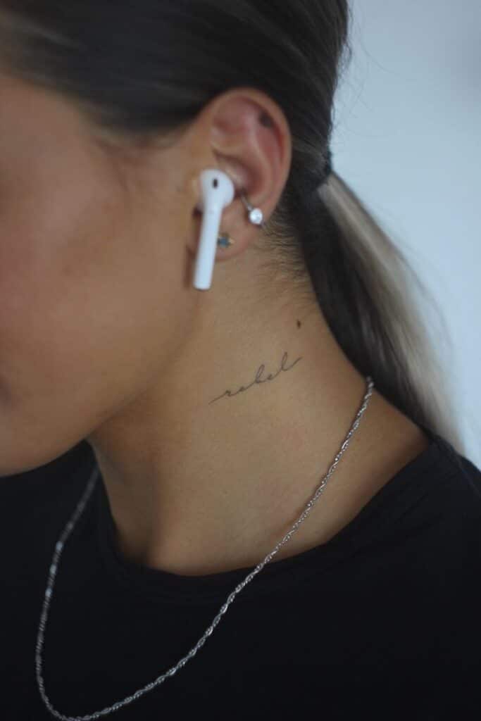 Woman with neck tattoo rebel, wearing earphones and earrings. Close-up profile with ponytail and silver chain.