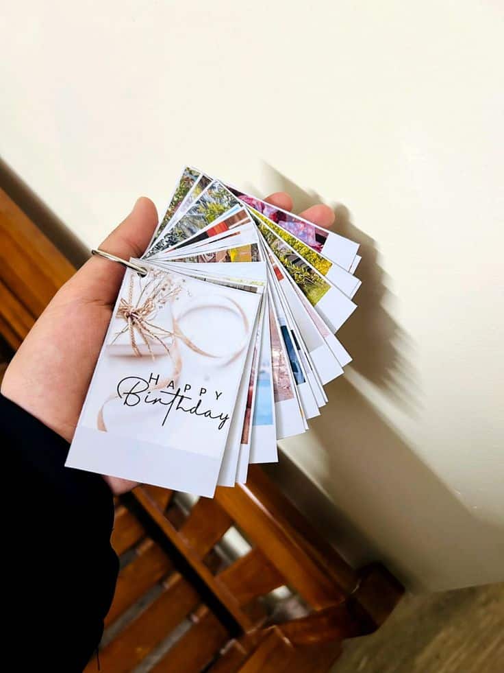 Hand holding a fan of colorful birthday cards against a beige background.