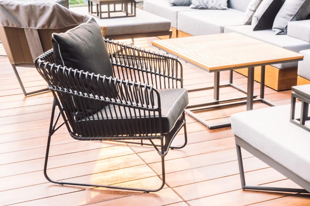 Outdoor patio with black wicker chair and wooden table on a sunny deck, ideal for modern lounging.