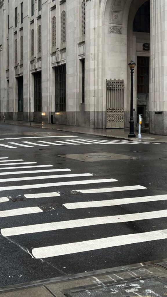 Empty city street with crosswalk and historic building facade on a rainy day.