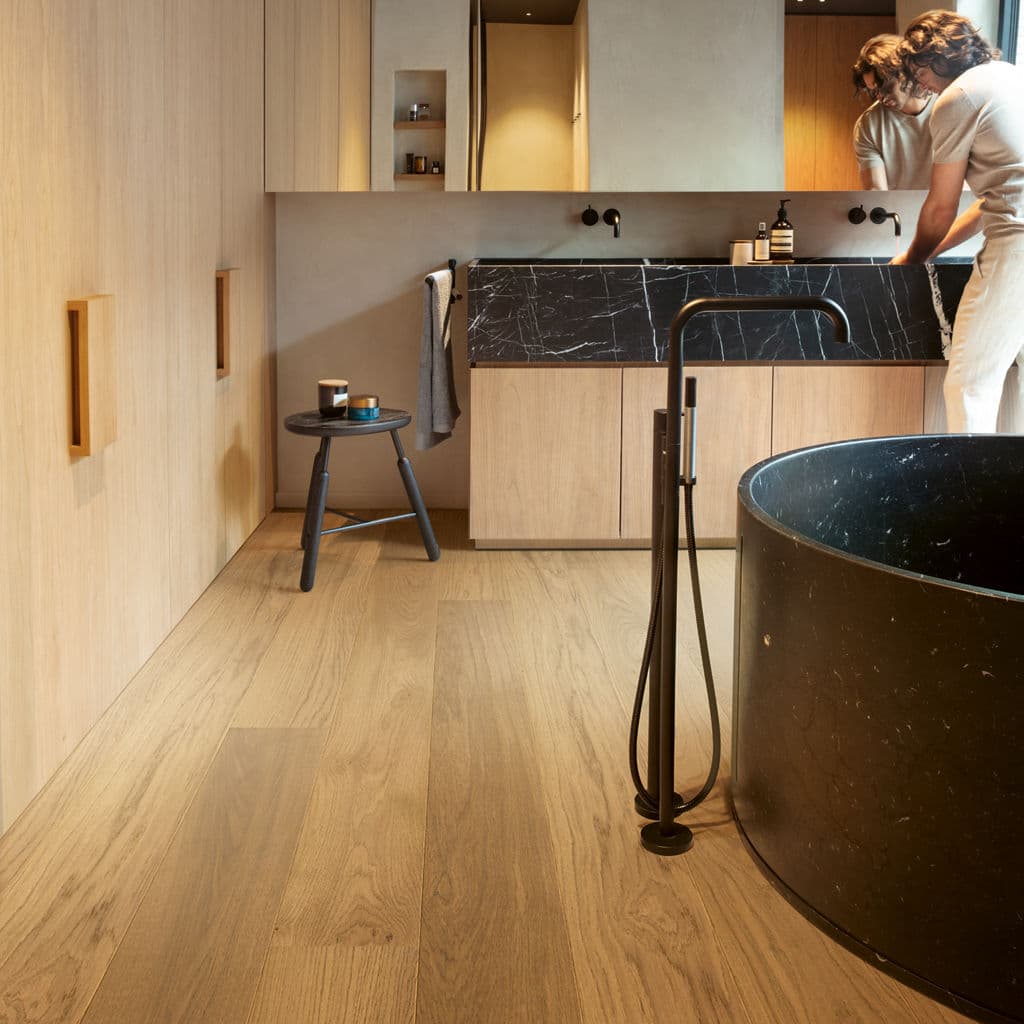 Modern bathroom with black marble tub, wooden flooring, and sleek vanity design for contemporary home decor.