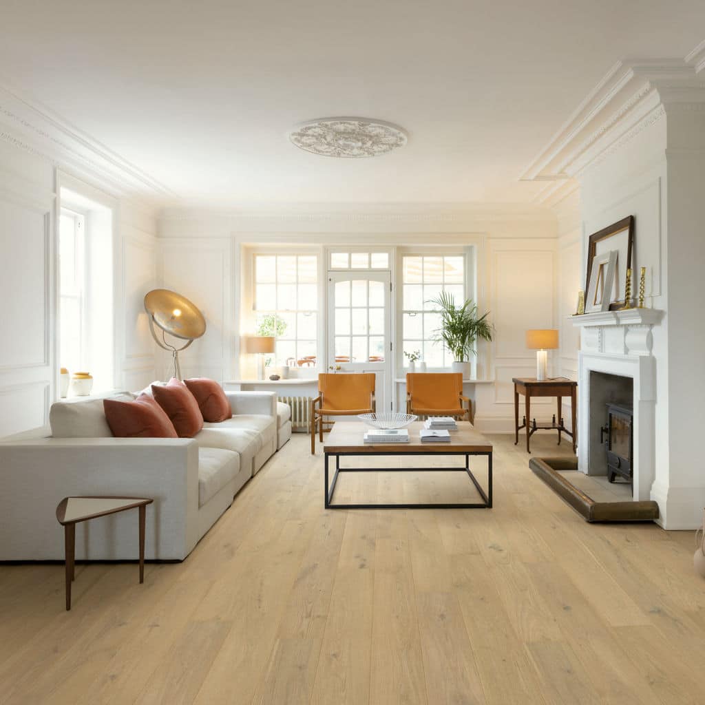 Modern living room with a white sofa, wooden flooring, and fireplace, featuring large windows and elegant decor.