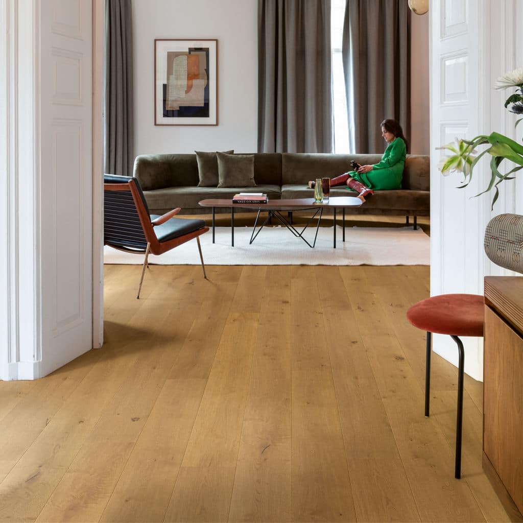 Stylish living room with hardwood floors, modern furniture, and a relaxing person on a green sofa.