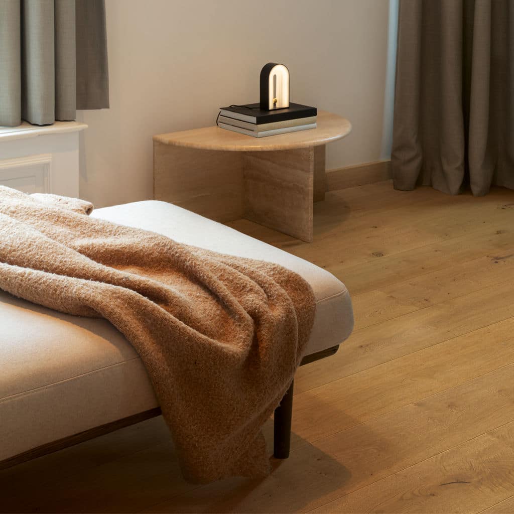 square lr-7 Minimalist bedroom with beige blanket on bed, wooden floors, side table, modern lamp, and curtains. | Sky Rye Design Minimalist bedroom with beige blanket on bed, wooden floors, side table, modern lamp, and curtains.