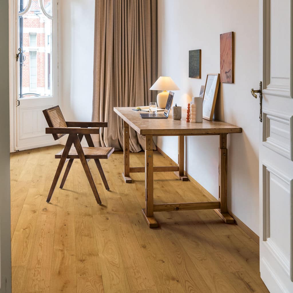 Minimalist home office with wooden desk, chair, and floor; laptop, lamp, decor; warm natural light from a tall window.