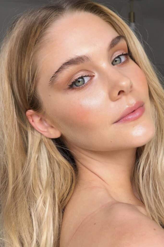 Close-up of a woman with clear skin and natural makeup, highlighting her green eyes and blonde hair.