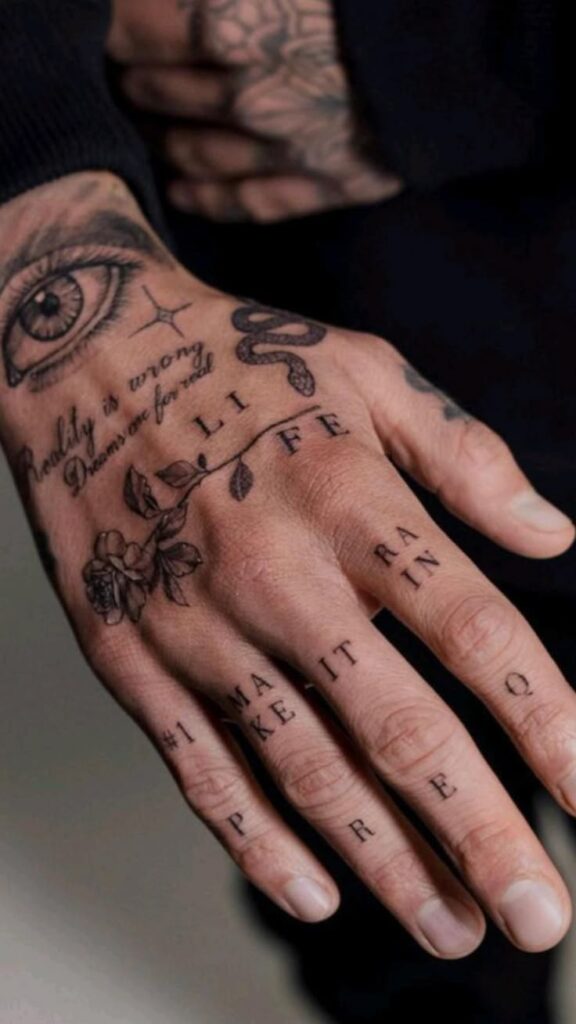 Hand with intricate tattoos, including an eye, floral design, and motivational words, expressing artistic style.