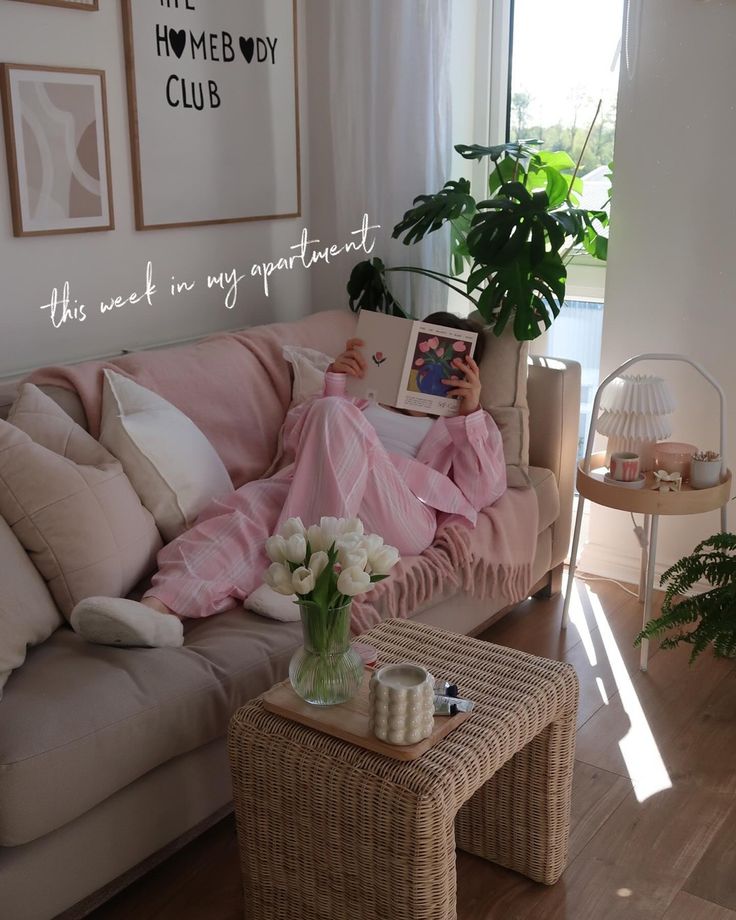 Cozy apartment living room with person reading on a couch, surrounded by plants and decor in soft lighting.