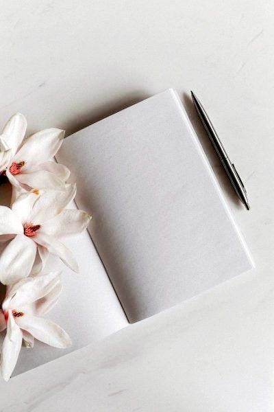 Open notebook with white flowers and a pen on a light surface, perfect for creative writing or journaling themes.