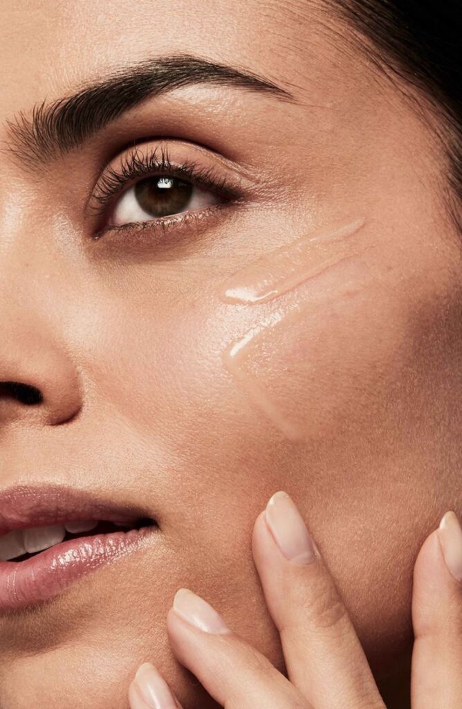 Woman applying skincare serum, highlighting smooth, radiant complexion and healthy skin texture.