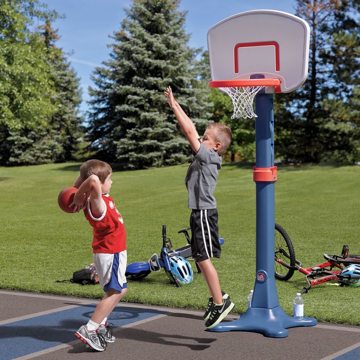 Kids playing basketball outdoors with a toy hoop and ball, surrounded by bicycles and greenery.