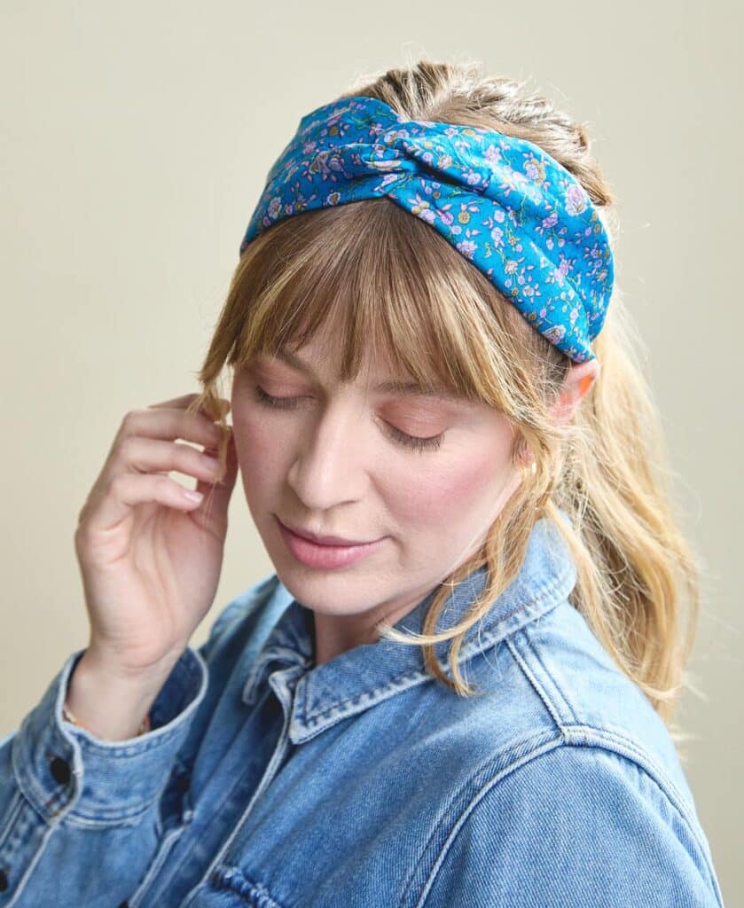 Woman wearing a denim jacket and a blue floral headband, looking down with closed eyes.