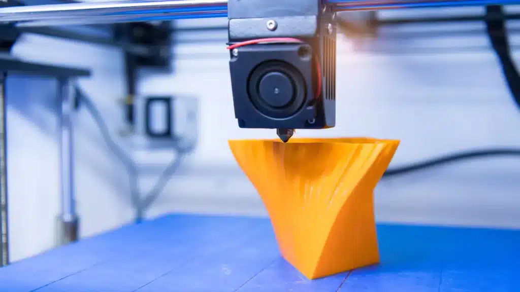 3D printer creating an orange vase, showcasing modern additive manufacturing technology in action.