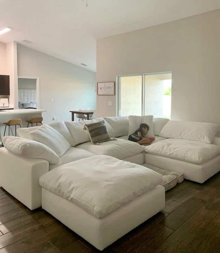 Cozy living room with a large white sectional sofa and a child resting, featuring a modern open kitchen design.
