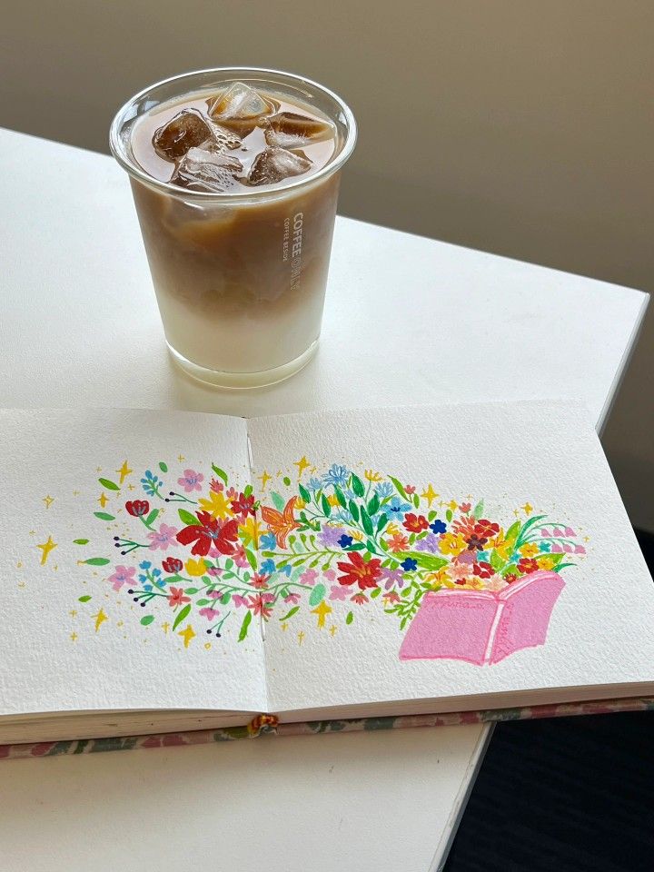 Ice latte and colorful flower illustration in open book on white table. Fresh and creative concept.