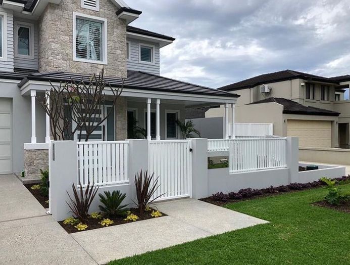 Modern two-story house with stone facade, white fence, and manicured lawn under a cloudy sky.