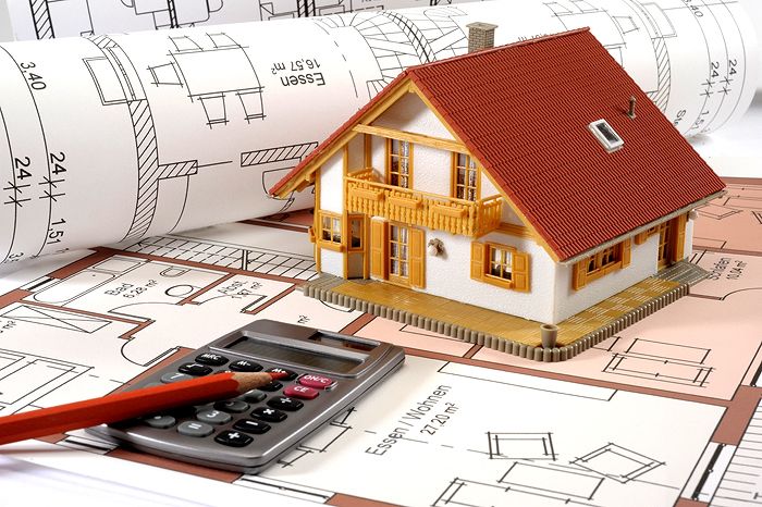 Model house on architectural blueprints with calculator and pencil, symbolizing real estate and home planning.