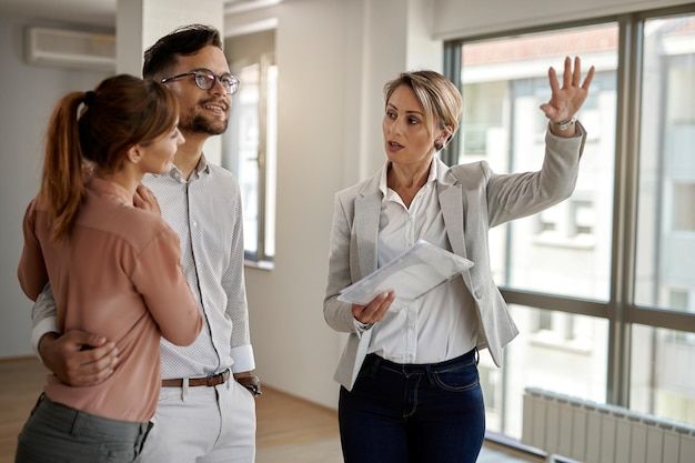 Real estate agent showing a new apartment to a couple, discussing features and layout near large windows.