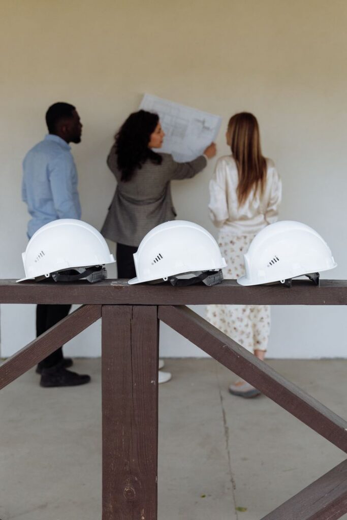 Three architects reviewing plans next to white construction helmets on a railing.