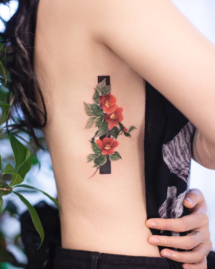 Floral tattoo design featuring red flowers and green leaves on a woman's side, emphasizing artistic body art.
