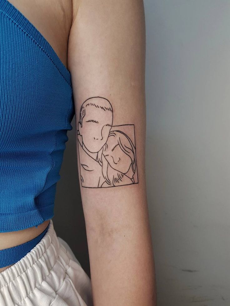Minimalist couple line art tattoo on upper arm, featuring two faces in a rectangular frame.