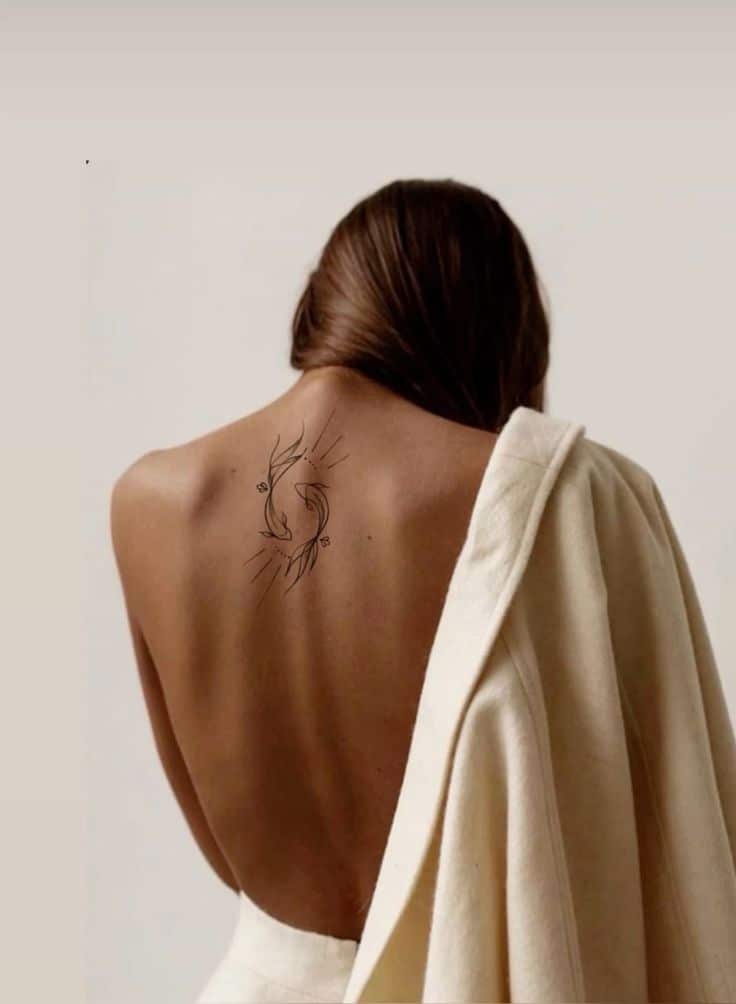 Back view of a woman with a minimalist tattoo in a neutral-toned draped outfit.