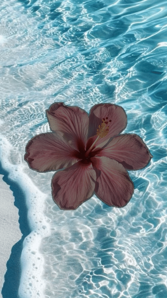 Pink hibiscus over shimmering beach waves and sandy shore.
