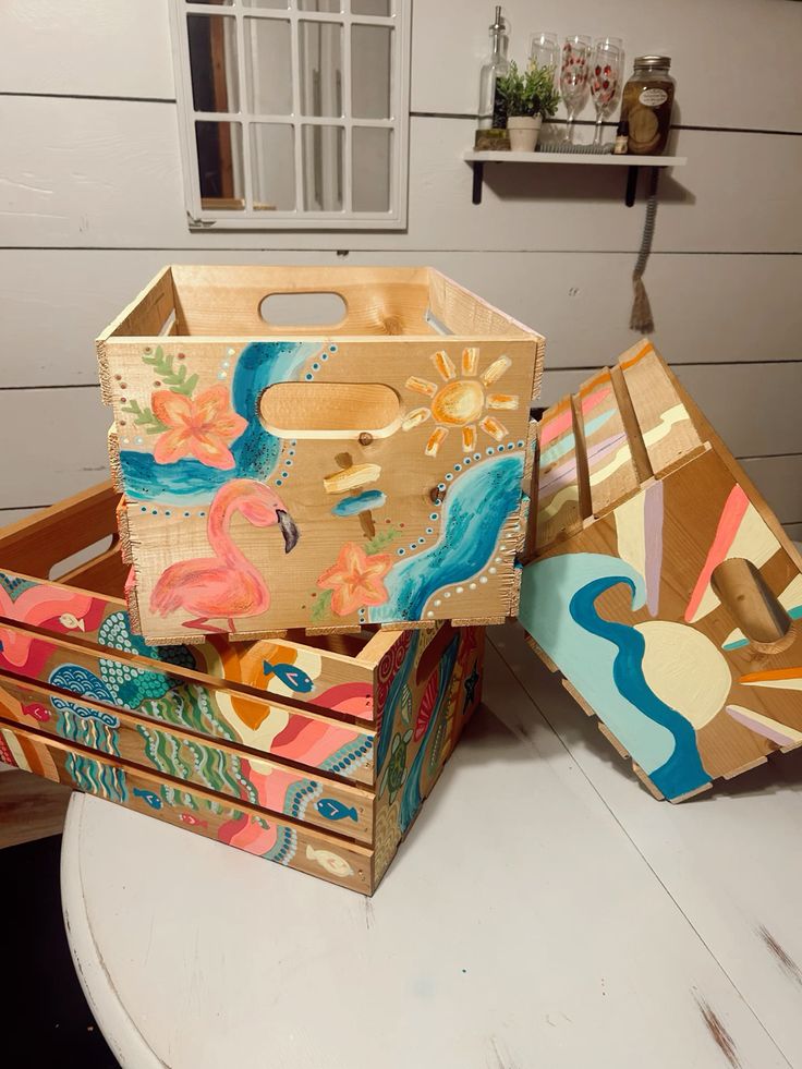 Hand-painted wooden storage boxes with vibrant sea and flamingo designs on a white table.