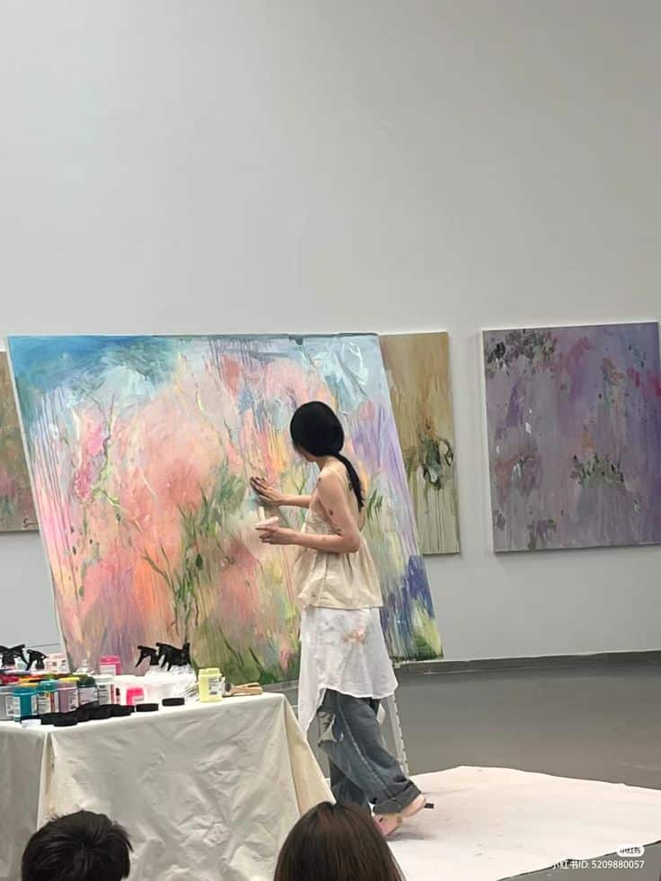 Artist painting a large abstract canvas in a studio, surrounded by art supplies.