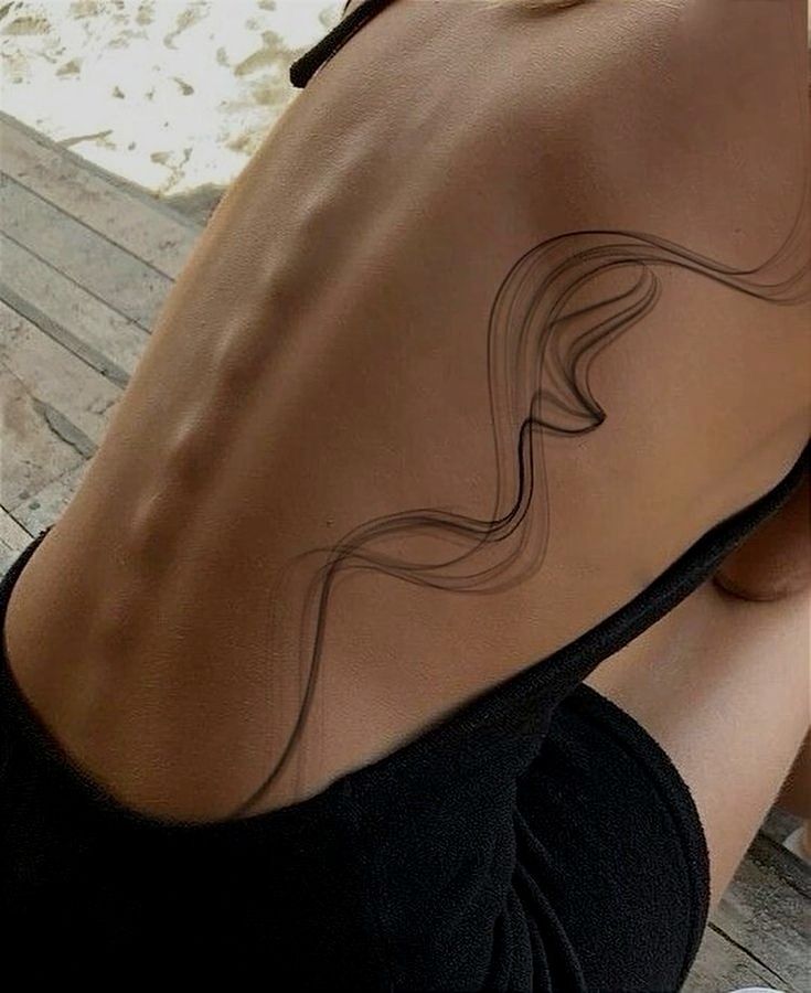 Close-up of a woman's back with a minimalist abstract tattoo, sunlight highlighting the tattoo's artistic curves.