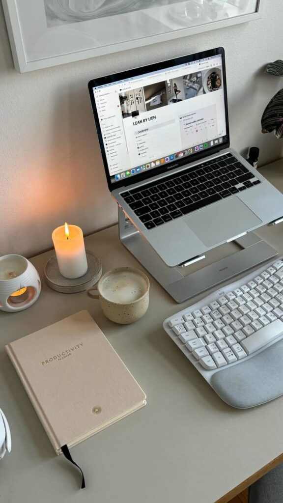 Modern workspace with laptop, keyboard, coffee, notebook, and lit candle for a cozy and productive environment.