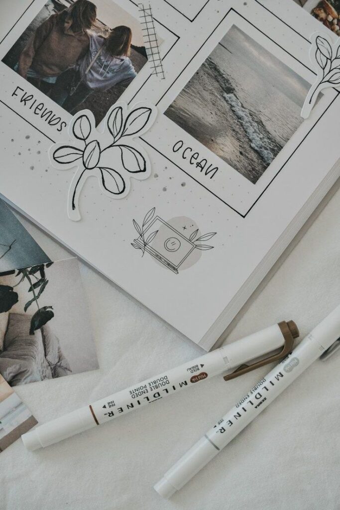 Scrapbook page with ocean and friends photos, artistic designs, and pens on a light surface.