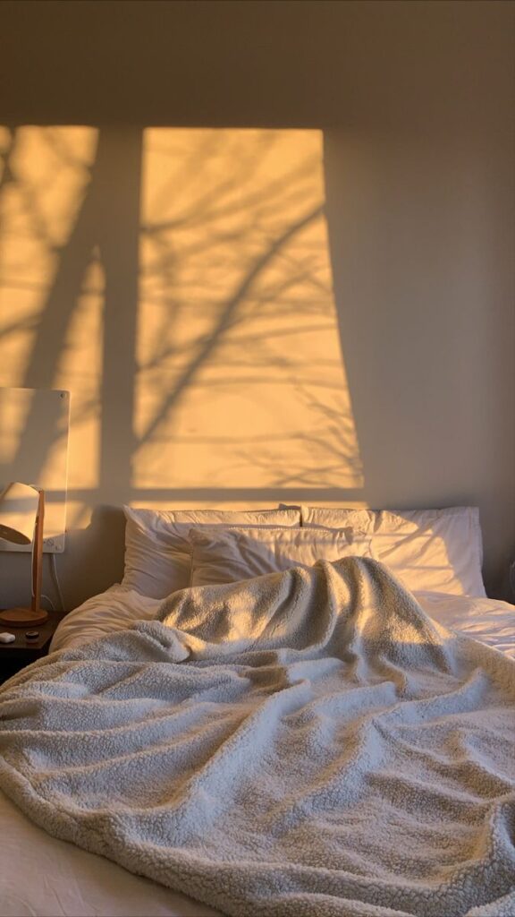Cozy bedroom with warm sunlight casting tree shadows on a wall above a bed with a soft blanket.