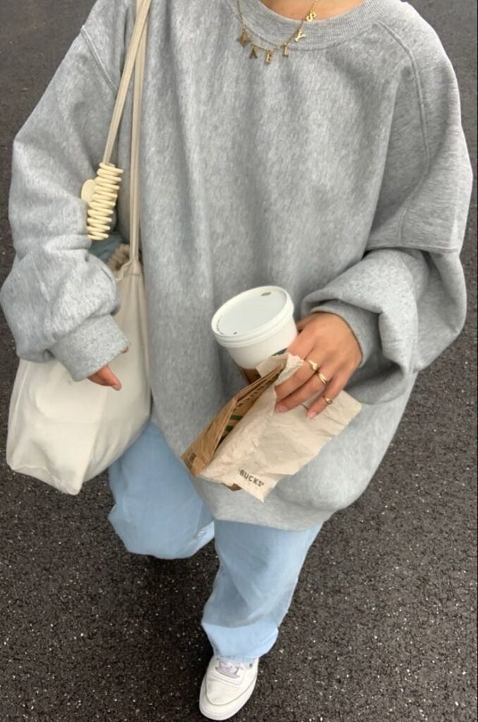 Person with a casual outfit holding a coffee cup, wearing a gray sweatshirt and light blue jeans.