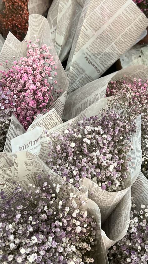 Bunches of pink and purple baby's breath flowers wrapped in newspaper, displayed at a market.