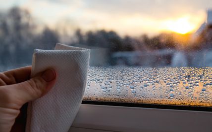 Что сделать чтобы окна зимой не потели_ пять народных средств Hand wiping condensation from a window with a cloth at sunrise, focusing on water droplets and outdoors scenery. | Sky Rye Design Hand wiping condensation from a window with a cloth at sunrise, focusing on water droplets and outdoors scenery.