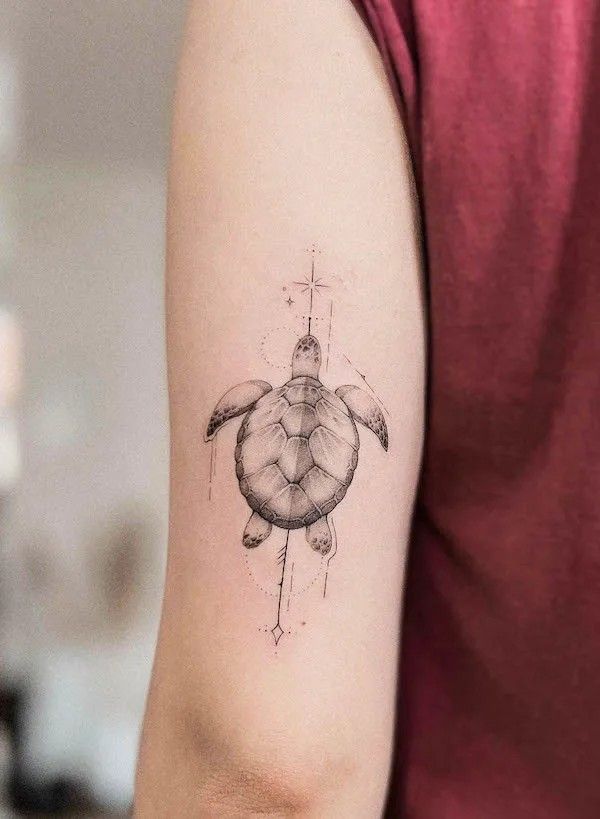 Sea turtle tattoo on arm with geometric and celestial accents, sleek black ink design on skin.