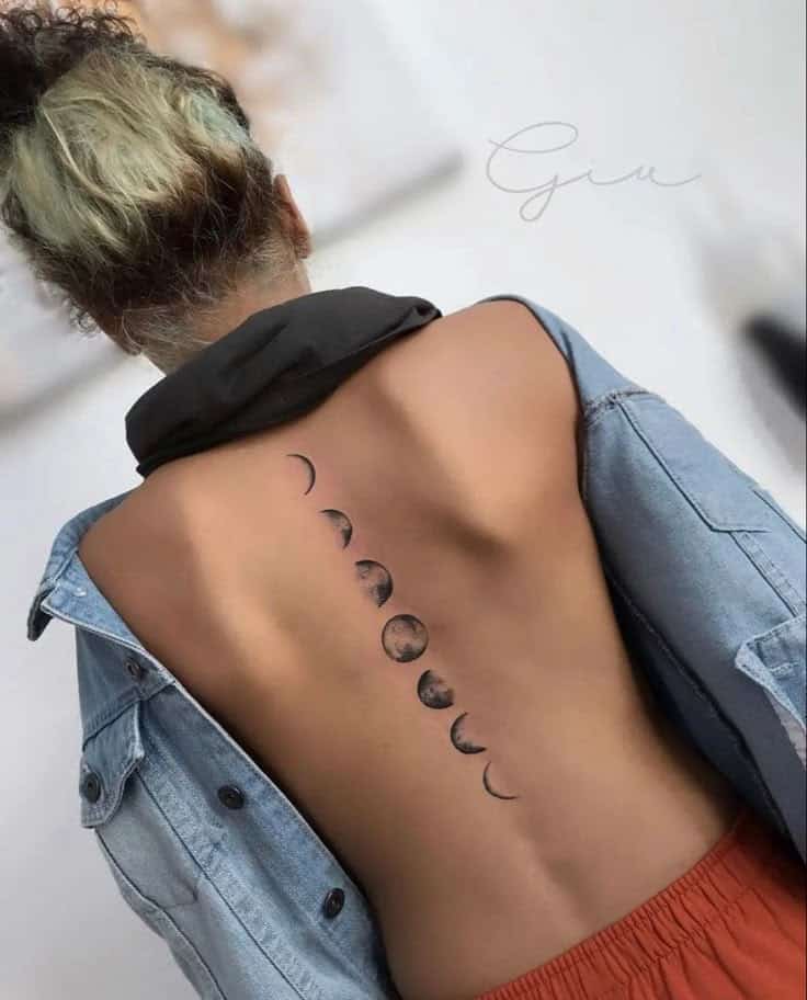 Back with lunar phase tattoo, denim jacket off-shoulder.